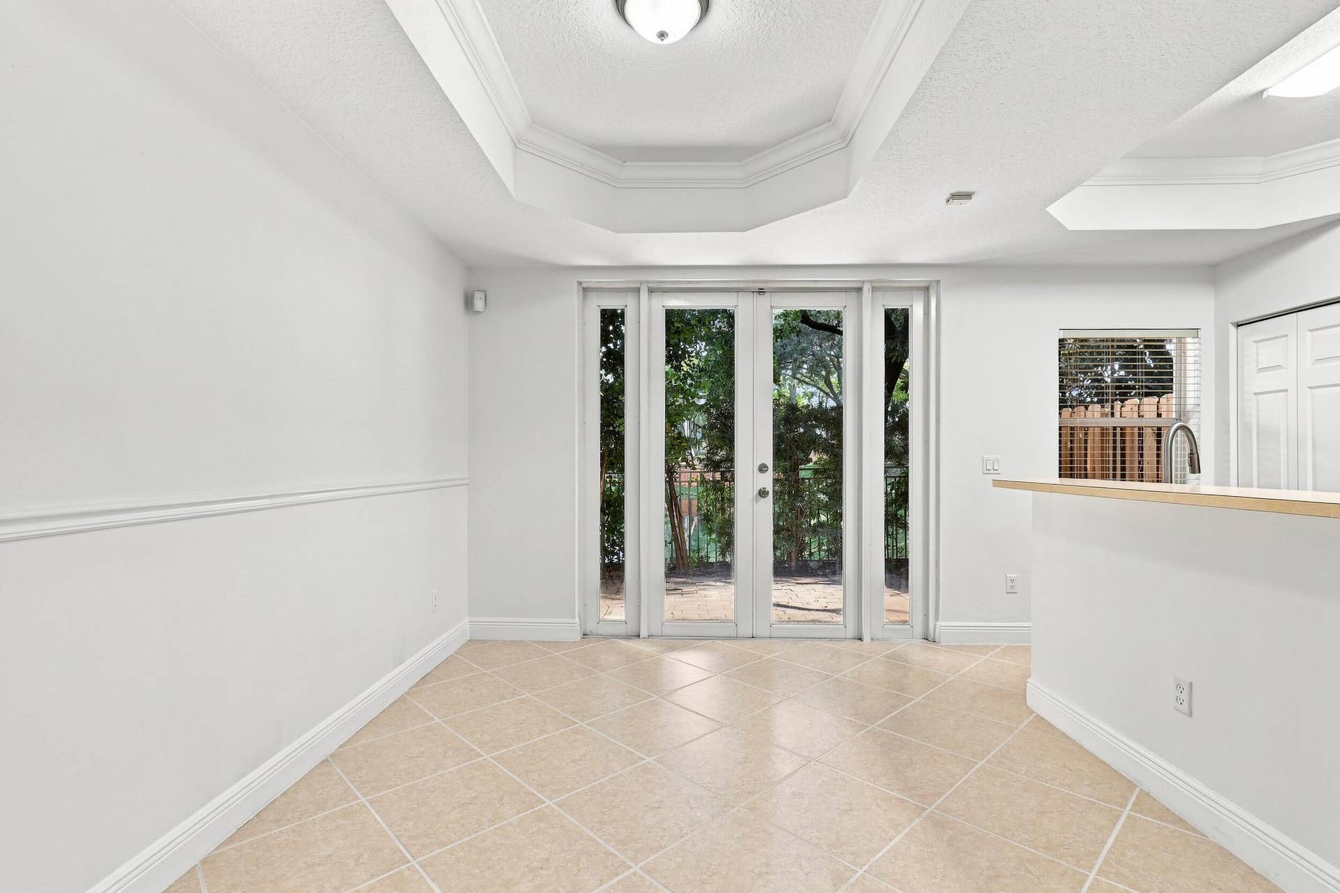 2107 Anchor Court, Fort Lauderdale, FL 33312 Bright dining area featuring tile flooring, a decorative tray ceiling with crown molding, and French doors that bring in natural light and provide direct access to the private outdoor patio. The open layout connects seamlessly with the kitchen for easy everyday living and entertaining.