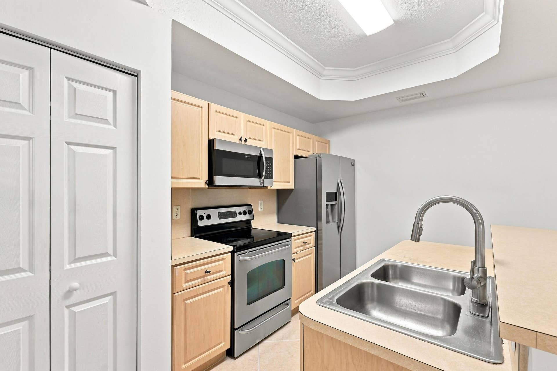 2107 Anchor Court, Fort Lauderdale, FL 33312 Bright, functional kitchen featuring ample cabinetry, stainless steel appliances, a double-basin sink, breakfast bar seating, and distinctive tray ceiling details. The open design provides an easy connection to the adjoining living and dining areas.
