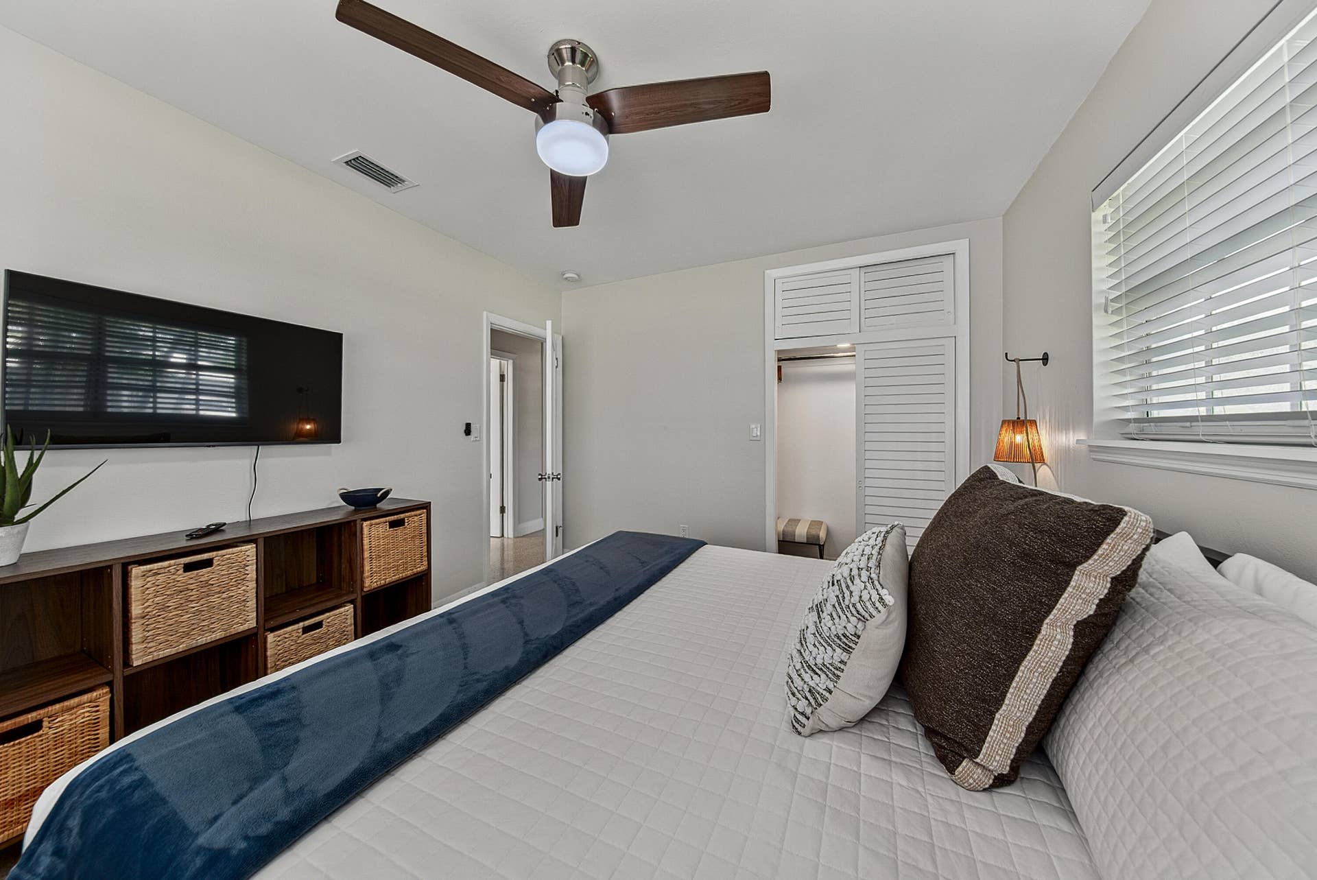 Ceiling fan with integrated lighting, wall-mounted light fixture, louvered closet doors, window with blinds, and light-toned wall paint