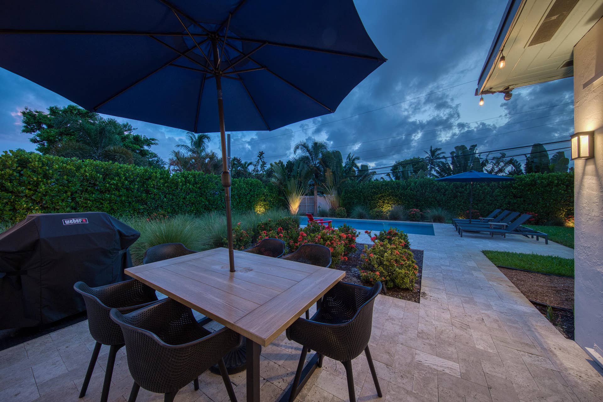 Outdoor living area featuring a wood-finish dining table, paver patio, swimming pool, and manicured landscaping