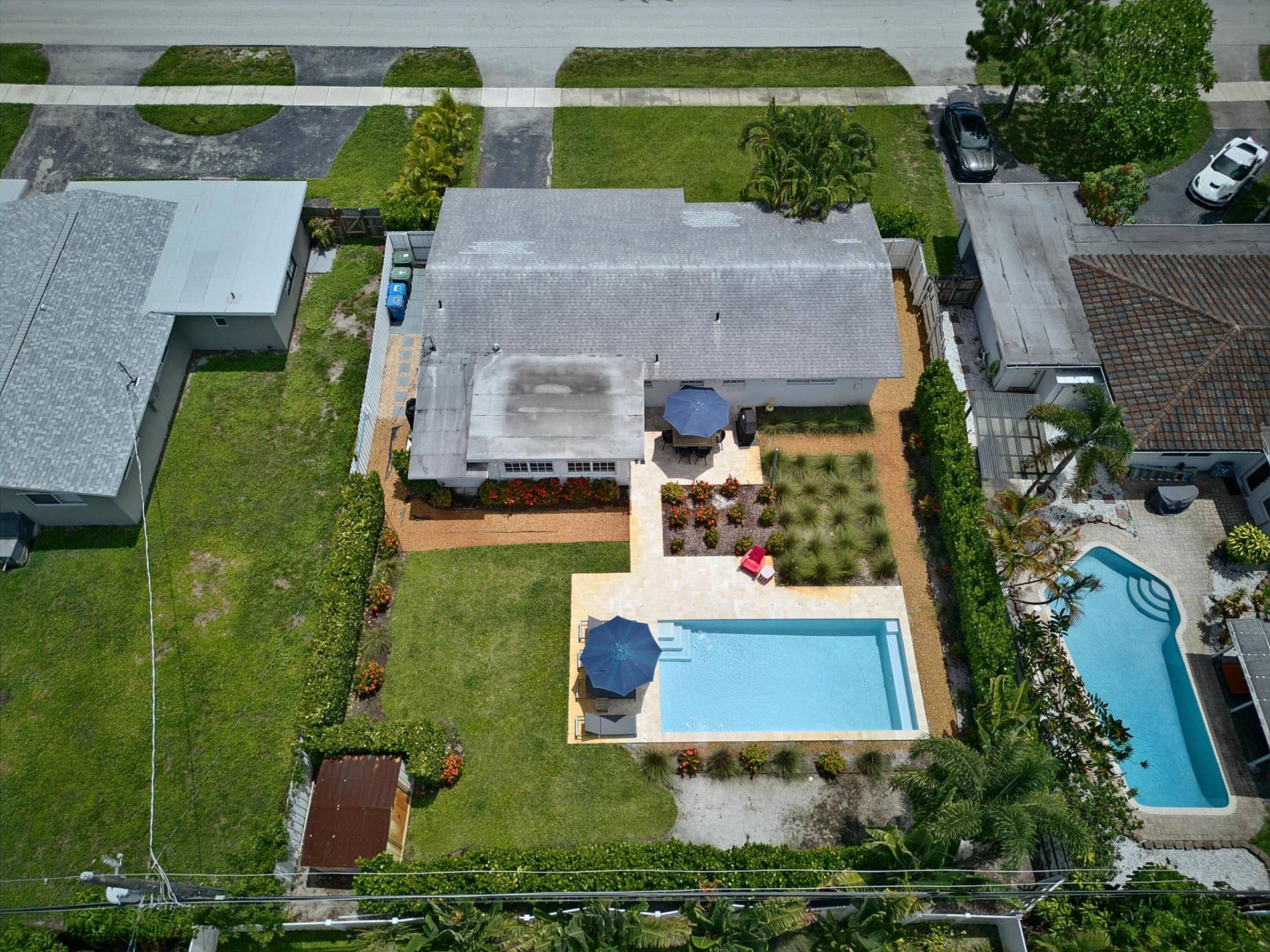 Aerial view of this residence showcasing a resort-style backyard featuring a heated swimming pool with surrounding concrete decking, mature landscaping with established trees, manicured lawn areas, and patio