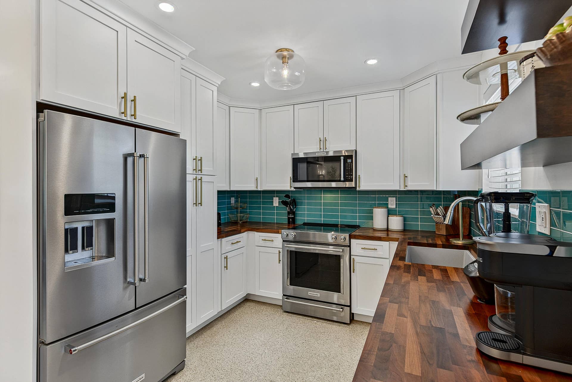 Modern kitchen featuring white shaker cabinetry with brushed nickel hardware, stainless steel French-door refrigerator and convection range, teal subway tile backsplash, wood-finish island countertop with seating, and recessed ceiling lighting throughout