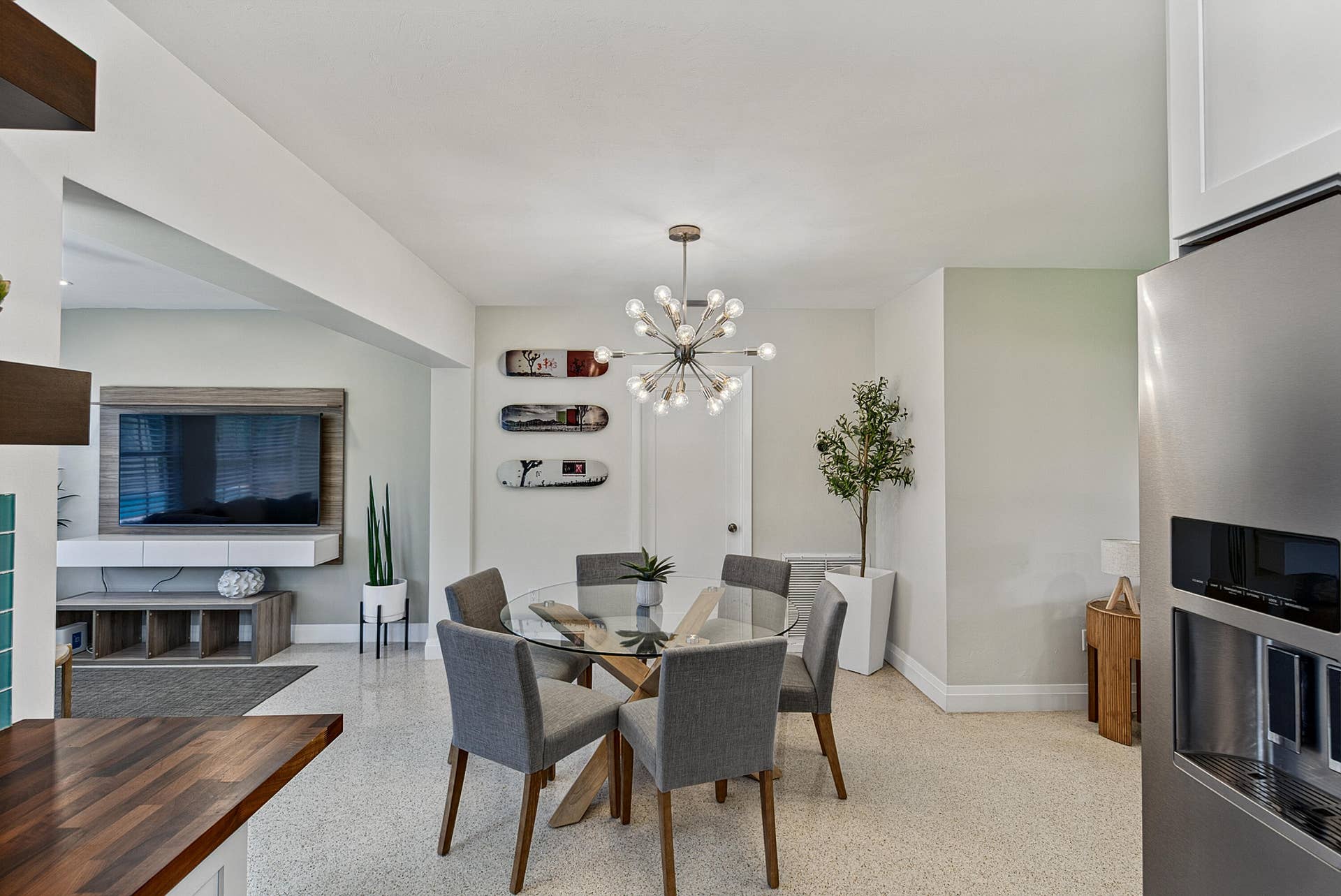 Open-concept living space featuring a modern Sputnik-style chandelier, a glass-top dining table, and light-toned terrazzo flooring