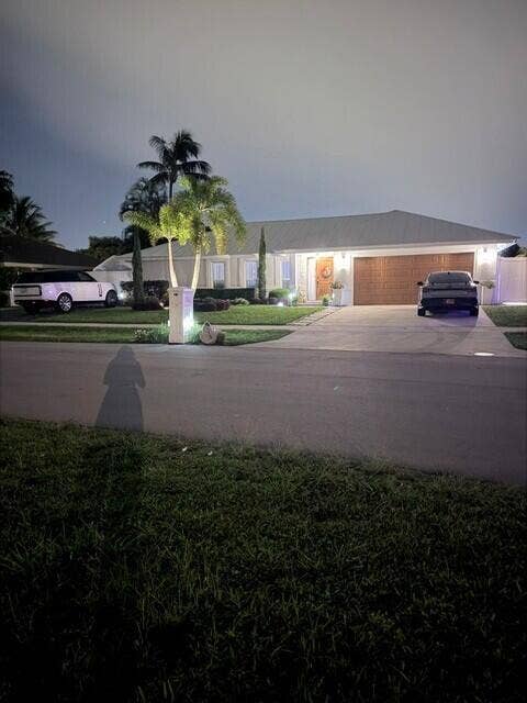 1201 SW 25TH Avenue, Boynton Beach, FL 33426 Beautifully illuminated at night, this inviting home showcases exceptional curb appeal with lush topical landscaping and a war, welcoming entrance. Elegant exterior lighting highlights the home's architecture and creates a striking first impression after sunset.