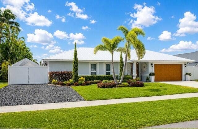 1201 SW 25TH Avenue, Boynton Beach, FL 33426 Front exterior featuring a wood-finish garage door, well-maintained lawn, and mature palm trees
