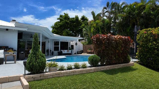 1201 SW 25TH Avenue, Boynton Beach, FL 33426 From the canal, this beautifully landscaped backyard showcases a sparkling pool framed by custom stone walls and lush tropical greenaery. The inviting outdoor living area creates a private setting perfect for entertaining.
