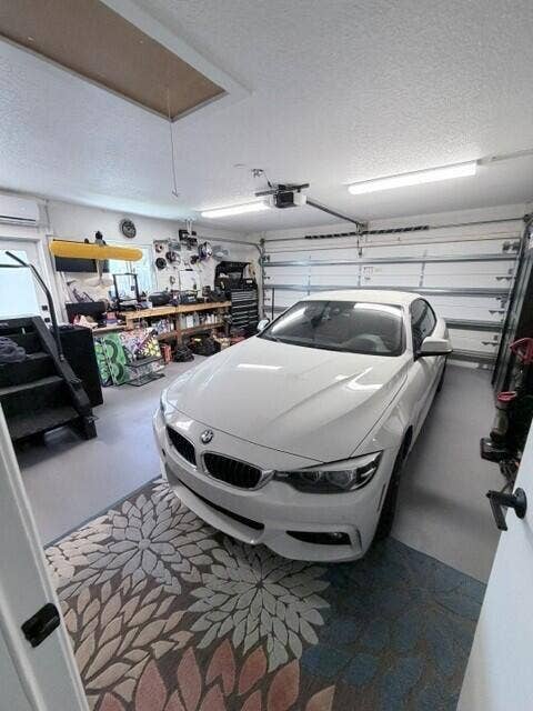 1201 SW 25TH Avenue, Boynton Beach, FL 33426 Attached two-car garage featuring a sectional garage door, overhead fluorescent lighting, a window-mounted air conditioning unit, and attic access