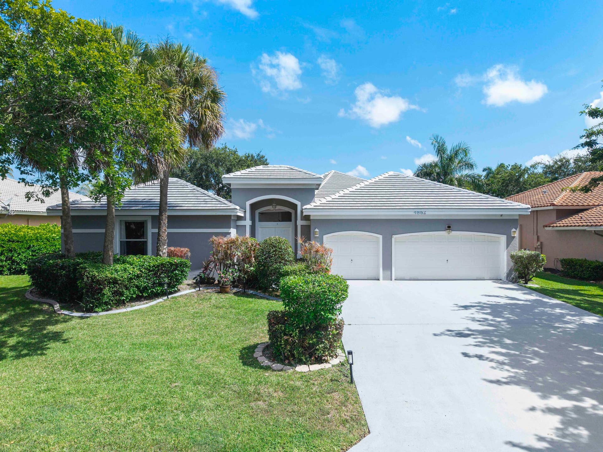 4862 Kensington Circle, Coral Springs, FL 33076 Stunning residence featuring a spacious three-car garage with white panel doors, elegant arched entryway with rounded architectural detailing, and a hipped roof design with tile accents