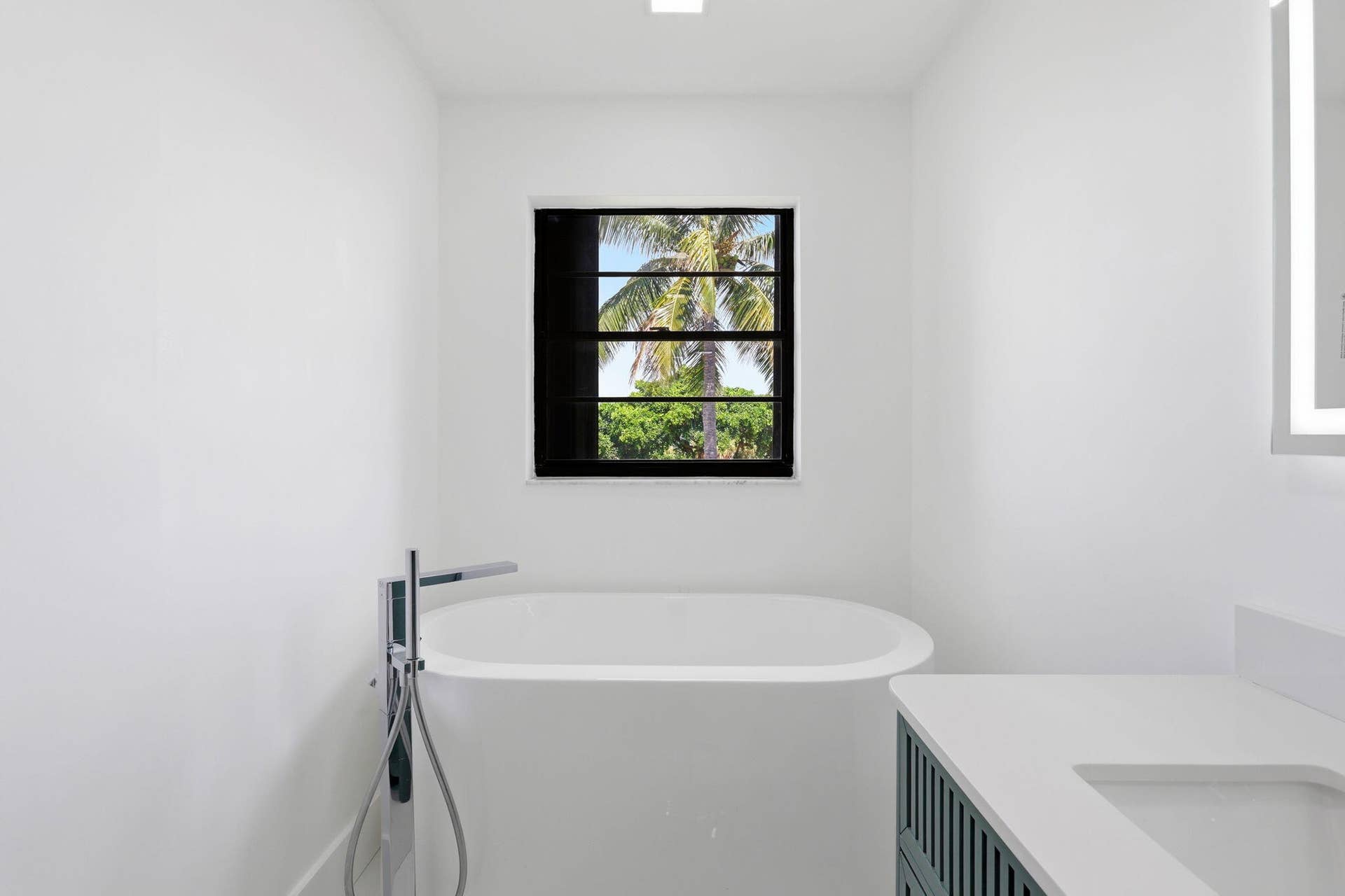 1222 Hillsboro Mile, #15, Hillsboro Beach, FL 33062 Freestanding soaking tub with floor-mounted chrome faucet, black-framed window, vanity with integrated sink, and illuminated mirror