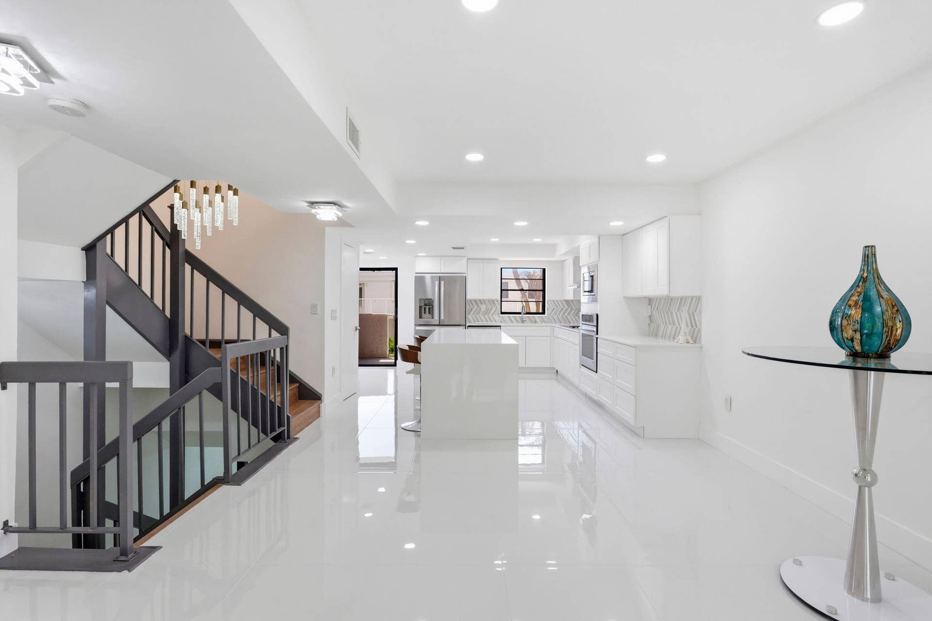 1222 Hillsboro Mile, #15, Hillsboro Beach, FL 33062 Sophisticated open-concept living space featuring polished light-finish flooring throughout, a curved staircase with metal railings and wood treads, recessed ceiling lighting, and a modern kitchen with white cabinetry and stainless steel appliances visible in the background