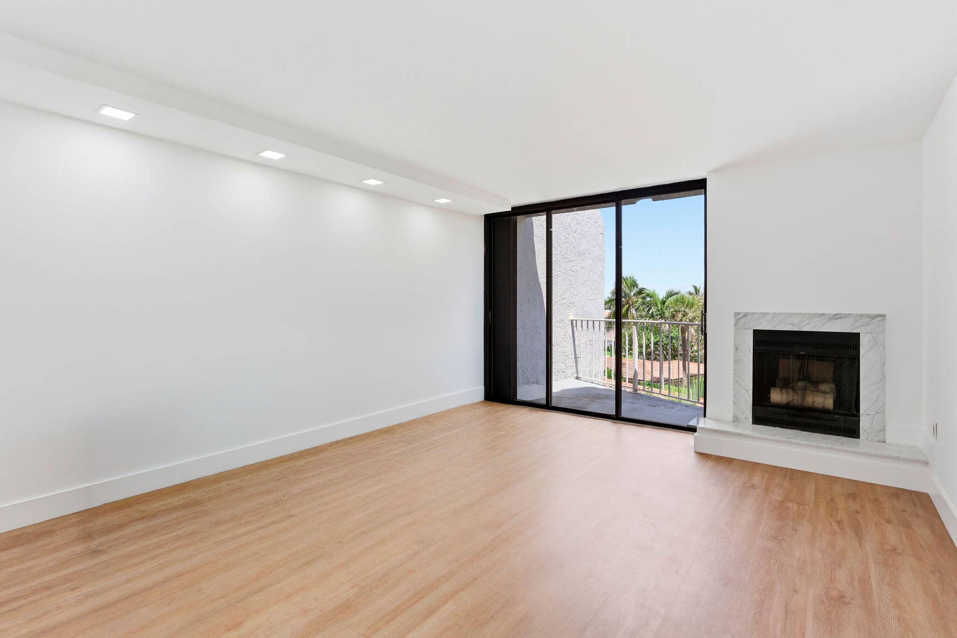 1222 Hillsboro Mile, #15, Hillsboro Beach, FL 33062 Spacious room with wood-finish flooring, a white marble fireplace, recessed ceiling lighting, and black framed glass sliding doors leading to a balcony with a white railing