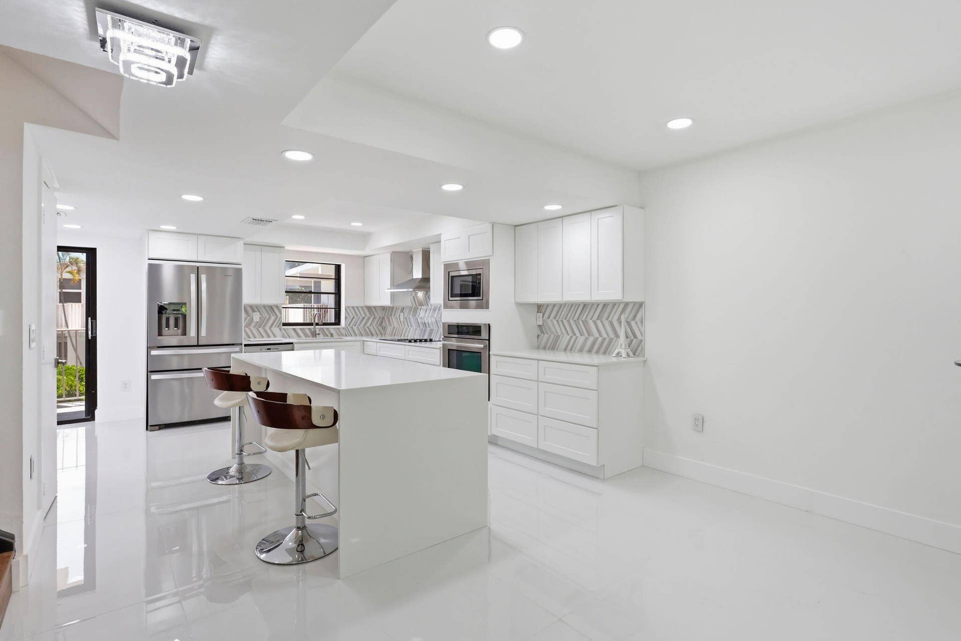 1222 Hillsboro Mile, #15, Hillsboro Beach, FL 33062 Contemporary kitchen featuring a large island, white cabinetry, stainless steel appliances, and a chevron tile backsplash