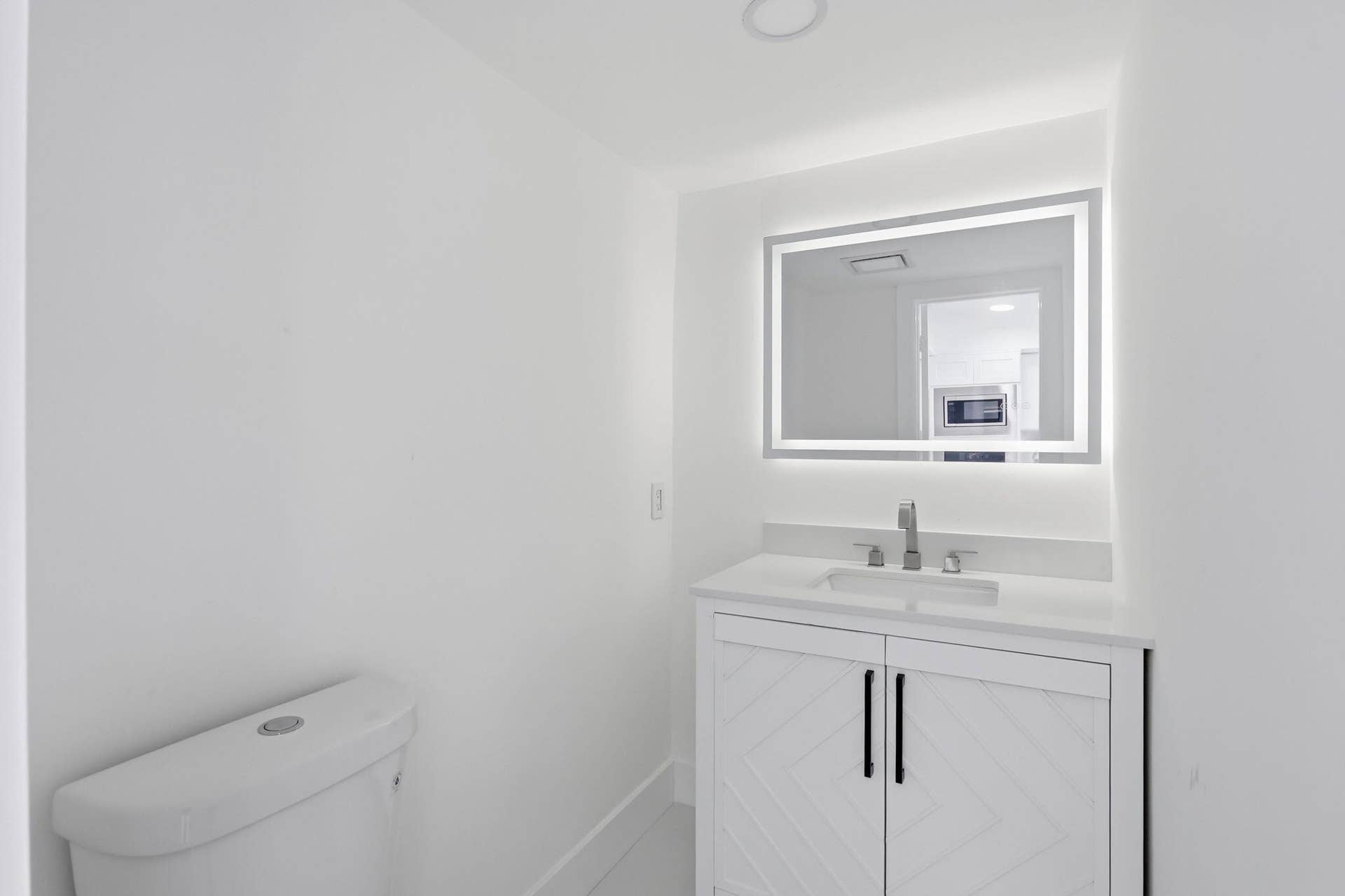 1222 Hillsboro Mile, #15, Hillsboro Beach, FL 33062 White vanity with textured cabinet doors and dark hardware, integrated rectangular sink, wall-mounted faucet, and illuminated mirror