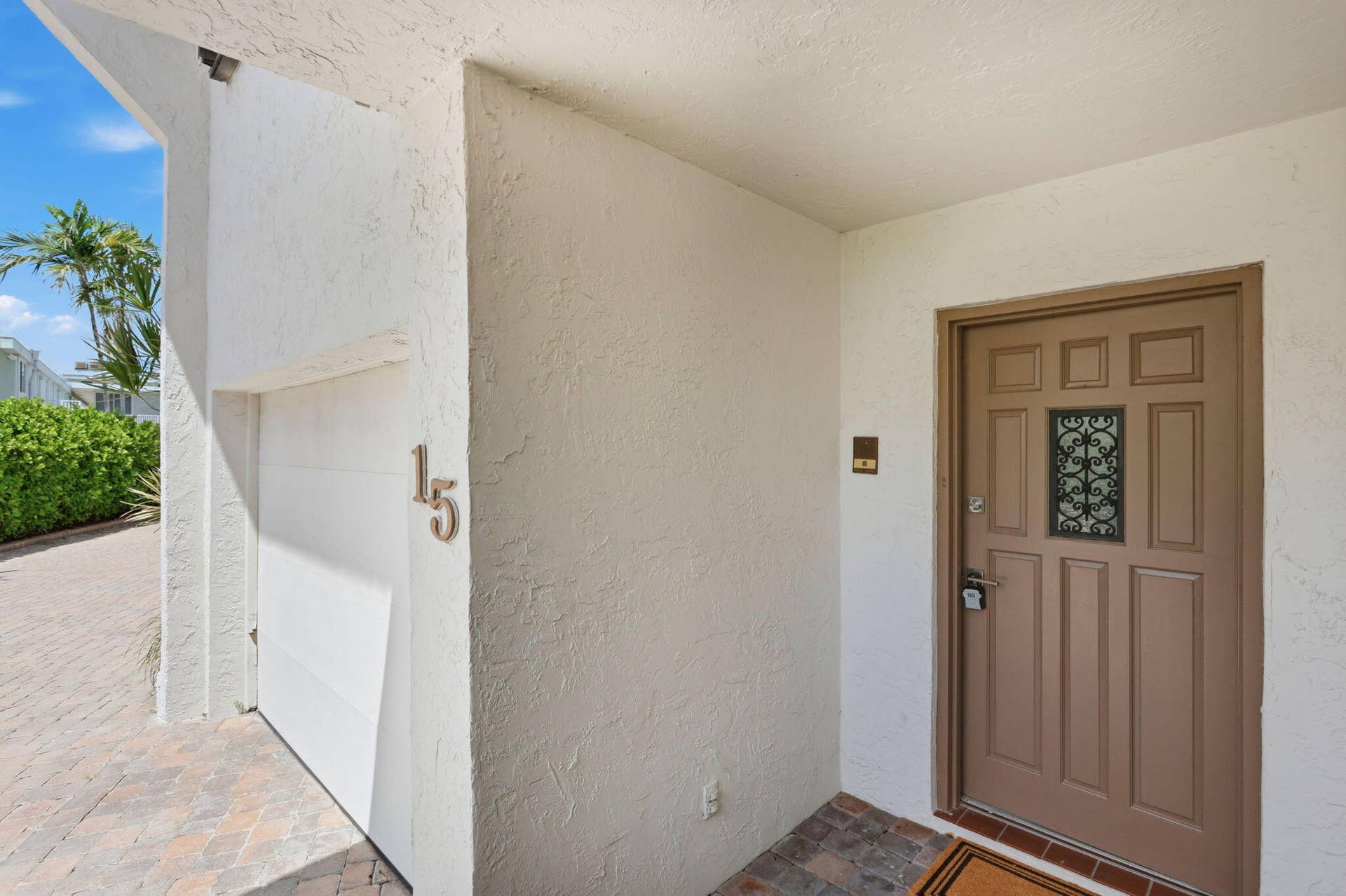 Textured exterior wall finish, paneled entry door with decorative ironwork, integrated garage door, and a brick paver driveway