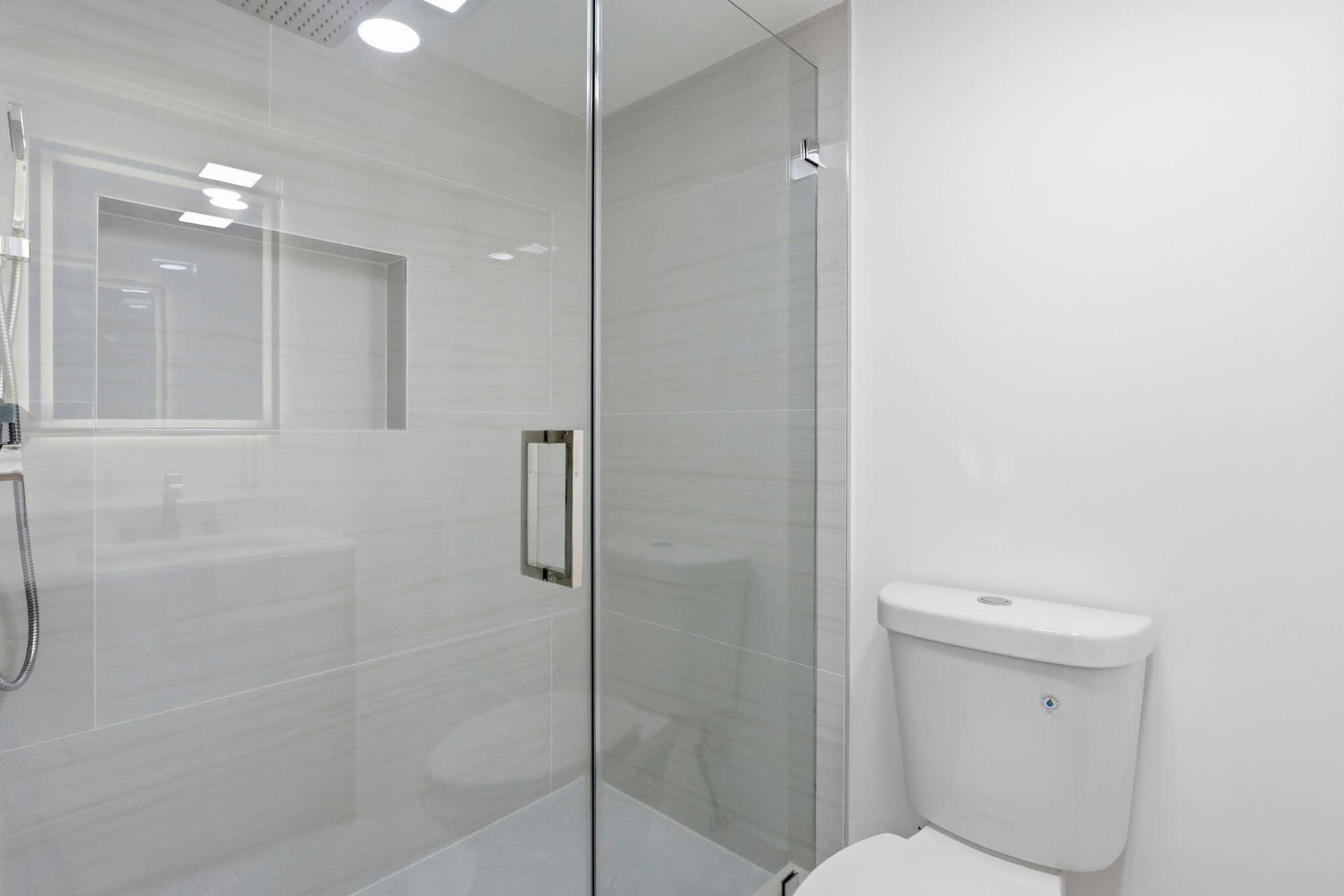 Glass-enclosed shower with a recessed niche, rain shower head, and an attached handheld shower fixture