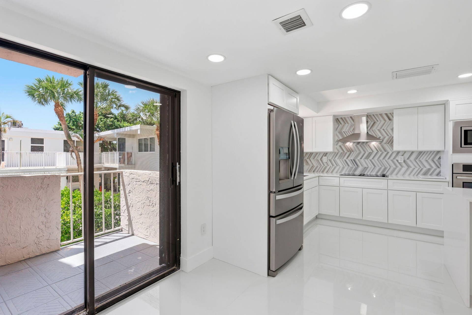 Modern kitchen featuring white cabinetry, stainless steel appliances, and a herringbone tile backsplash, dining area