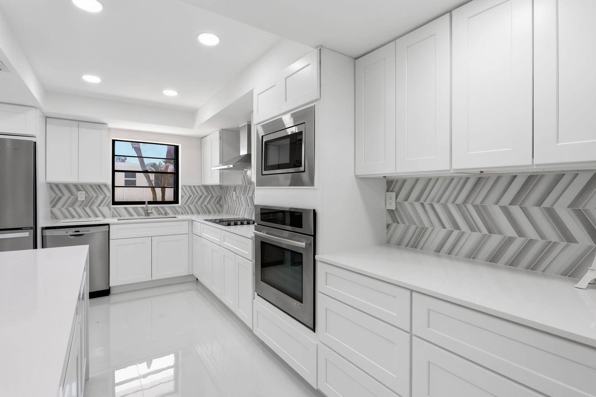 White cabinetry, stainless steel appliances, herringbone-patterned backsplash, recessed lighting, and a window above the sink