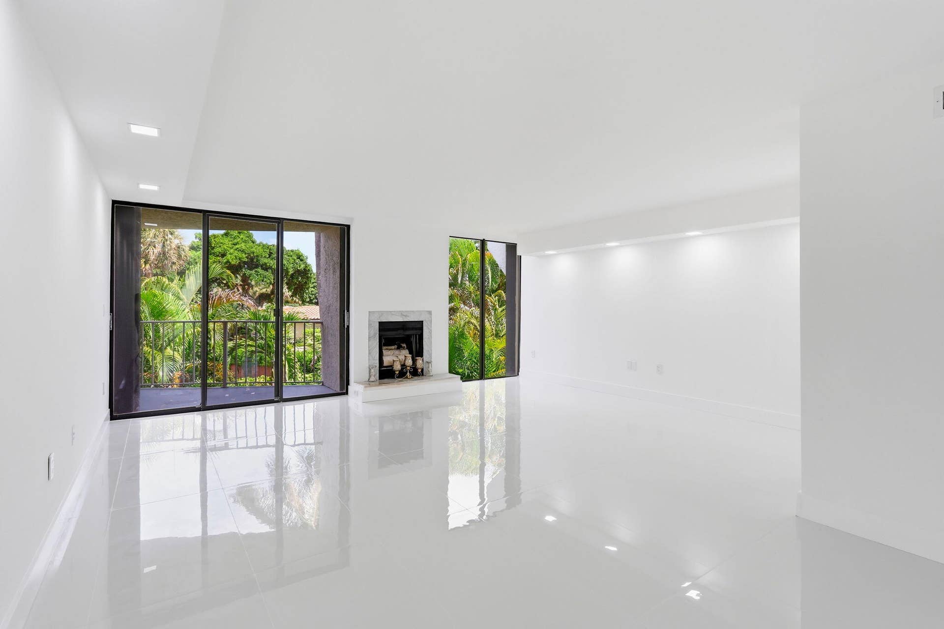 Expansive living area featuring reflective flooring, a decorative fireplace, and large sliding glass doors leading to an outdoor balcony with railings