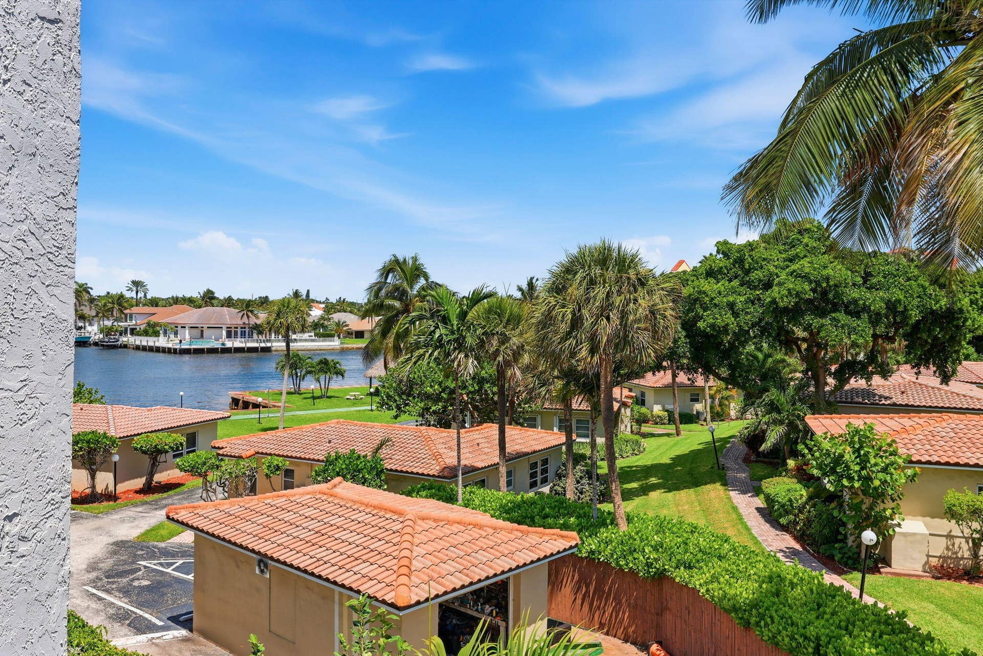 Waterfront property with mature palm trees, manicured lawns, and terracotta-tiled roofs