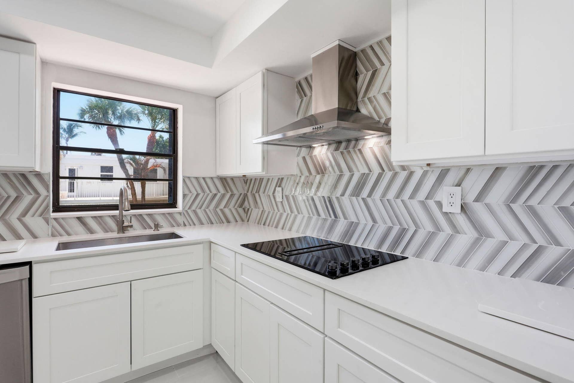 White shaker-style cabinetry with minimalist hardware, white countertops, and a full-height chevron-patterned tile backsplash