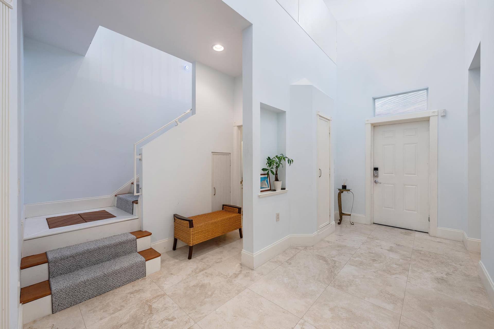 Two-story foyer with high ceilings, light-toned tiled flooring, and a stairway featuring carpeted treads and white risers