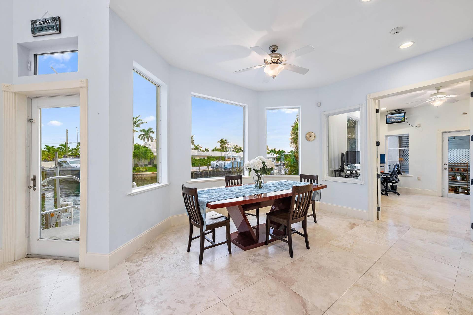 Waterfront dining area with large windows, light-toned tile flooring, and ceiling fan