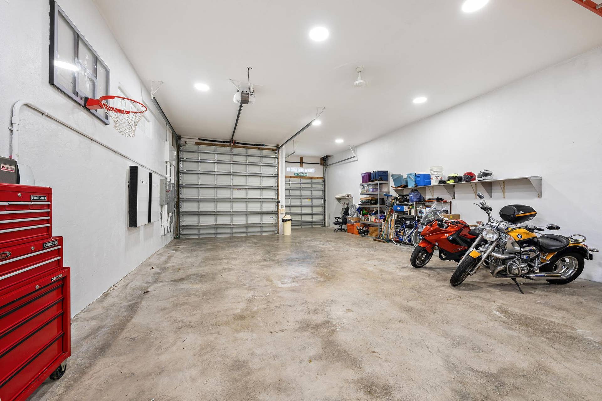 Spacious garage featuring polished concrete flooring, overhead lighting, wall-mounted storage cabinetry, a basketball hoop, and ample room for multiple vehicles and recreational equipment