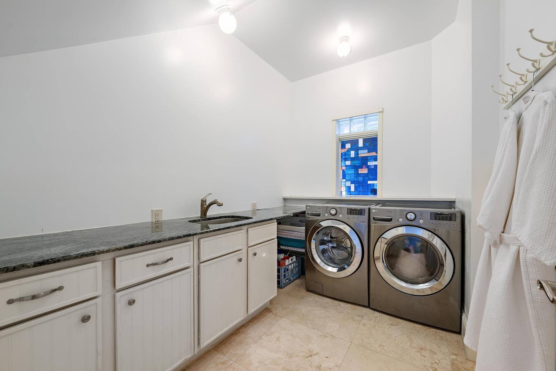 Laundry area with a vaulted ceiling, durable tile flooring, and a long countertop with an undermount sink