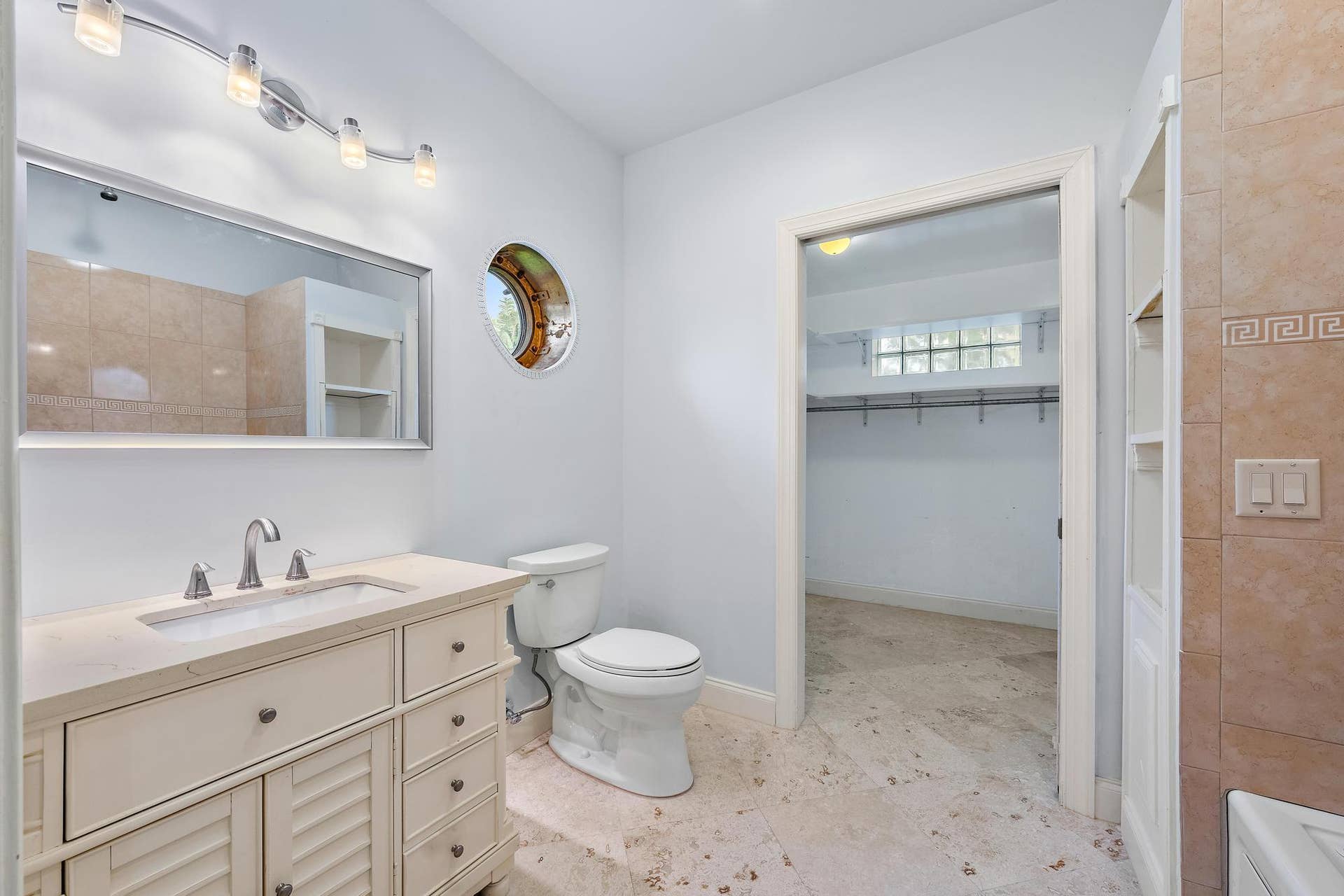 Vanity with integrated sink, contemporary wall-mounted lighting, recessed mirror, and a unique circular window