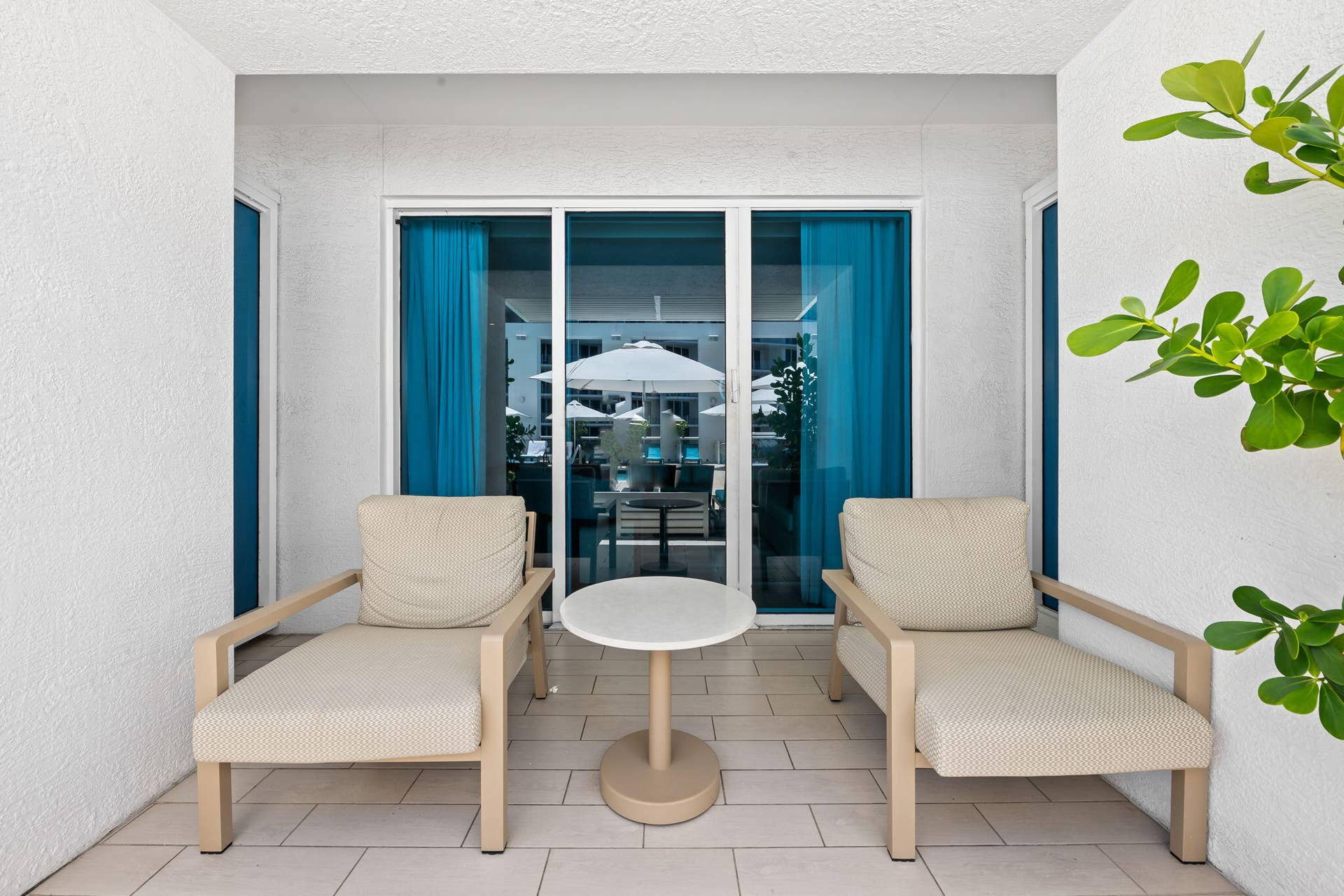 Covered outdoor lounge featuring dual wood-frame armchairs with cushioned seating, a round pedestal side table, and tile flooring