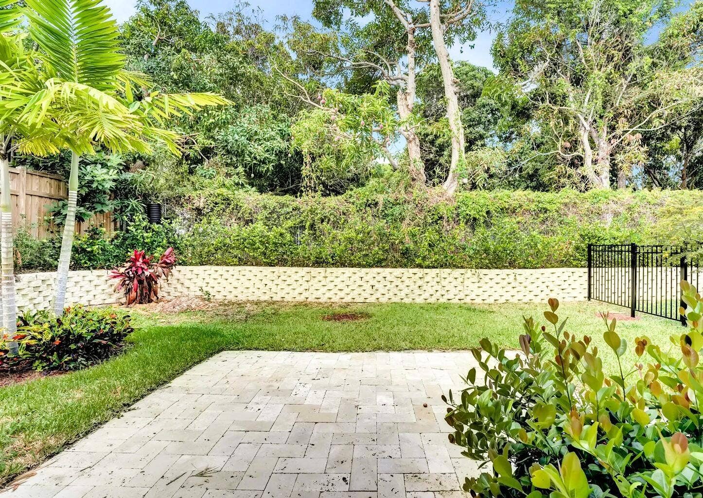 2517 Oceanview Avenue E, Delray Beach, Delray Beach, FL 33444 Paver patio with a lush lawn, privacy fence, mature trees, and a decorative retaining wall