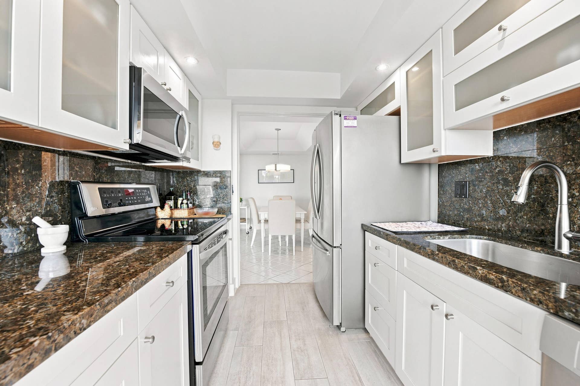 3589 S Ocean Boulevard, #808, South Palm Beach, FL 33480 Galley kitchen featuring white cabinetry with frosted glass inserts, dark speckled countertops, and a matching full-height backsplash