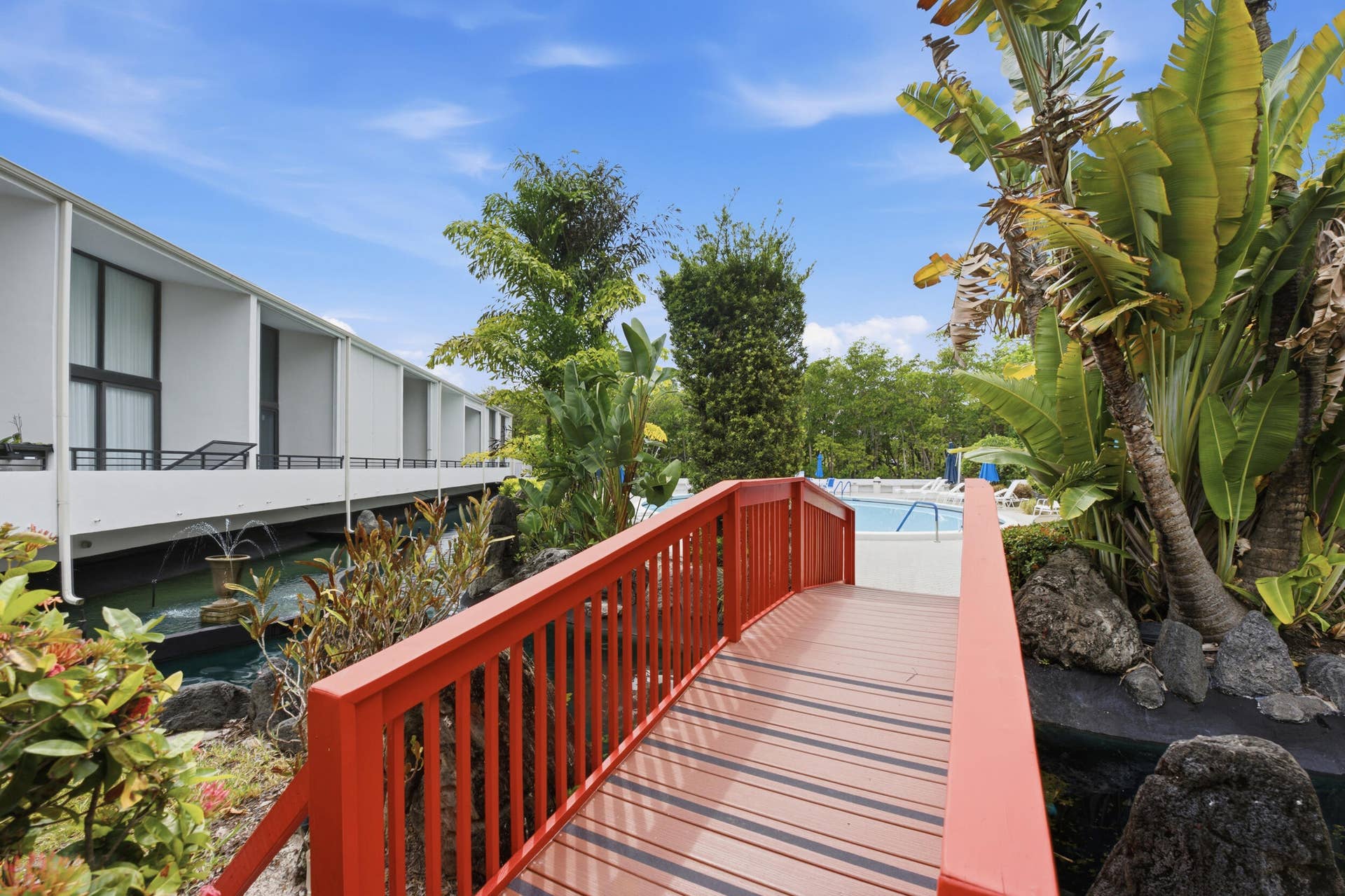 3589 S Ocean Boulevard, #808, South Palm Beach, FL 33480 Vibrant red pedestrian bridge over a water feature, bordered by lush tropical landscaping
