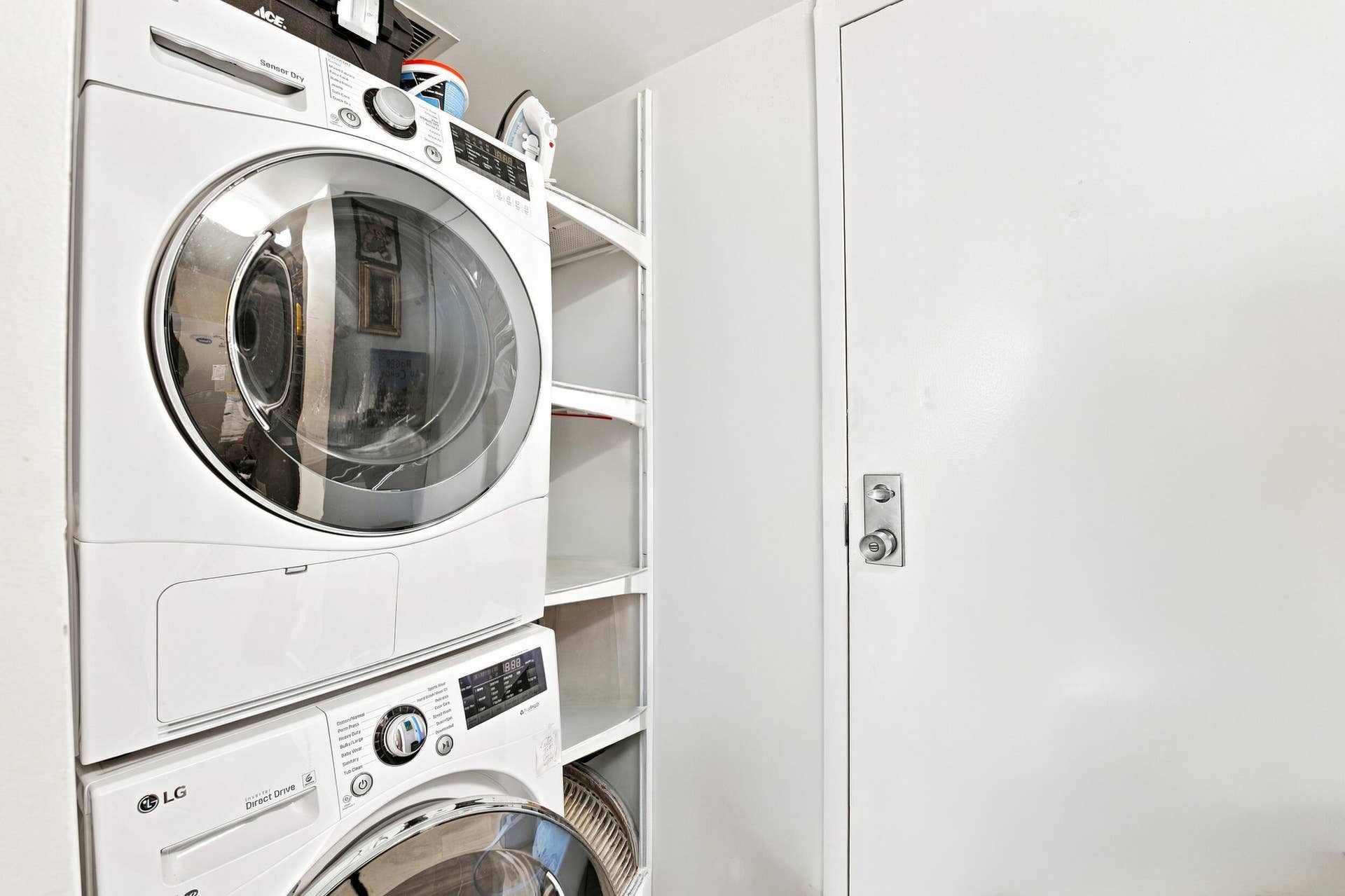 3589 S Ocean Boulevard, #808, South Palm Beach, FL 33480 Dedicated laundry area featuring a stacked washer and dryer, integrated shelving, and a solid white door with brushed chrome hardware