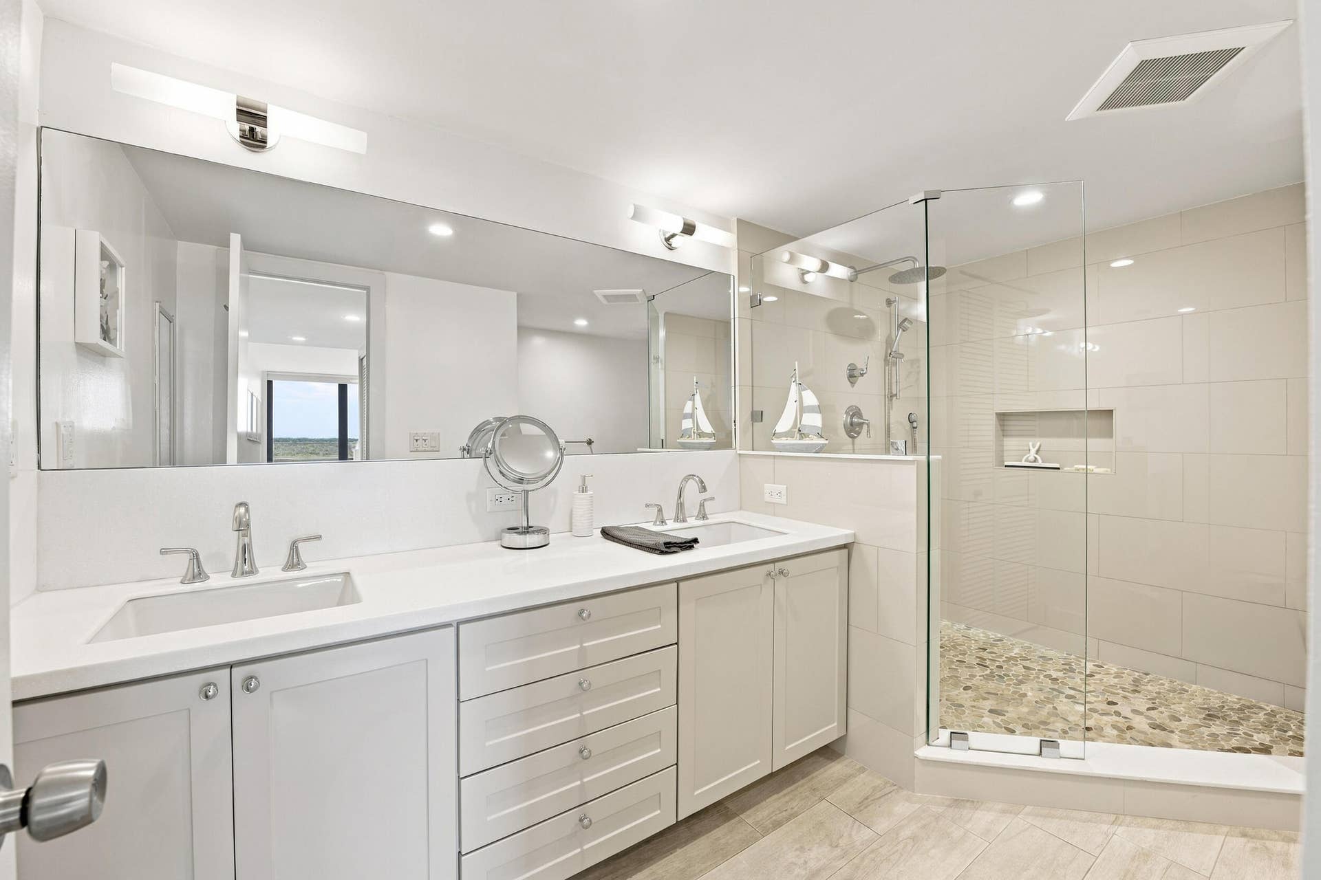 3589 S Ocean Boulevard, #808, South Palm Beach, FL 33480 Bathroom featuring a dual vanity with undermount sinks and chrome fixtures, a large frameless mirror, and a glass-enclosed shower with a pebble floor and tiled walls