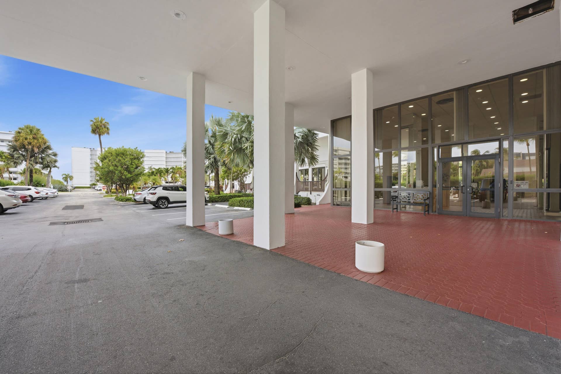3589 S Ocean Boulevard, #808, South Palm Beach, FL 33480 Covered driveway featuring a red brick paver surface, expansive glass storefront, and white structural columns