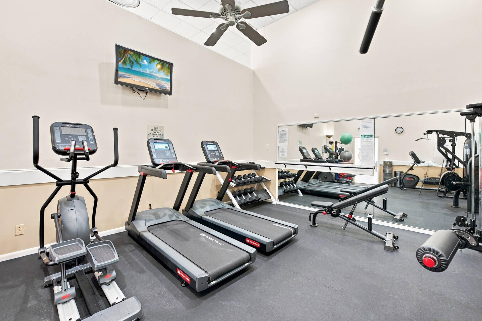 3589 S Ocean Boulevard, #808, South Palm Beach, FL 33480 Fitness room featuring vaulted ceilings, a ceiling fan, wall-mounted television, full-wall mirror, and rubber flooring