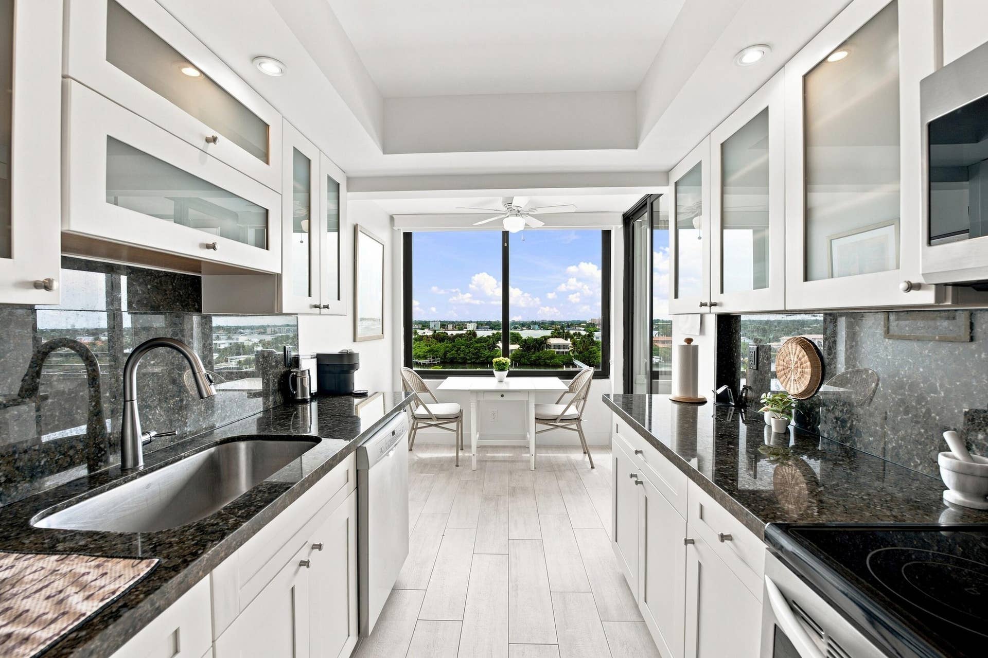3589 S Ocean Boulevard, #808, South Palm Beach, FL 33480 Galley kitchen with unique window featuring white cabinetry, dark stone countertops, and a stainless steel sink with a gooseneck faucet