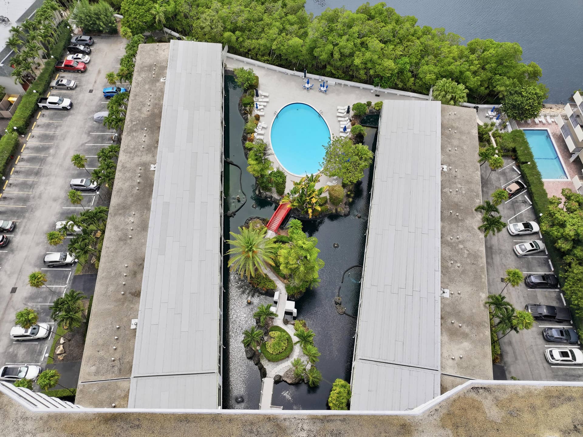 3589 S Ocean Boulevard, #808, South Palm Beach, FL 33480 Rooftop recreational space featuring a circular swimming pool, lush landscaping with palm trees, a decorative red bridge, and a water feature