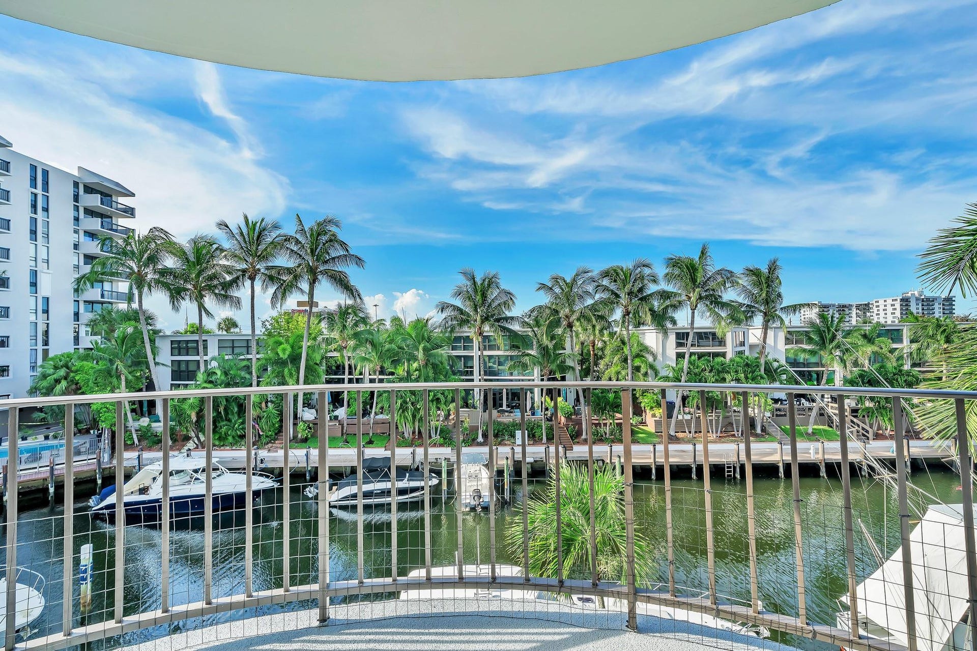 3051 NE 48TH Street, #301, Fort Lauderdale, Fort Lauderdale, FL 33308 Curved balcony with metal railing overlooking a waterway with boats, palm trees, and residential buildings