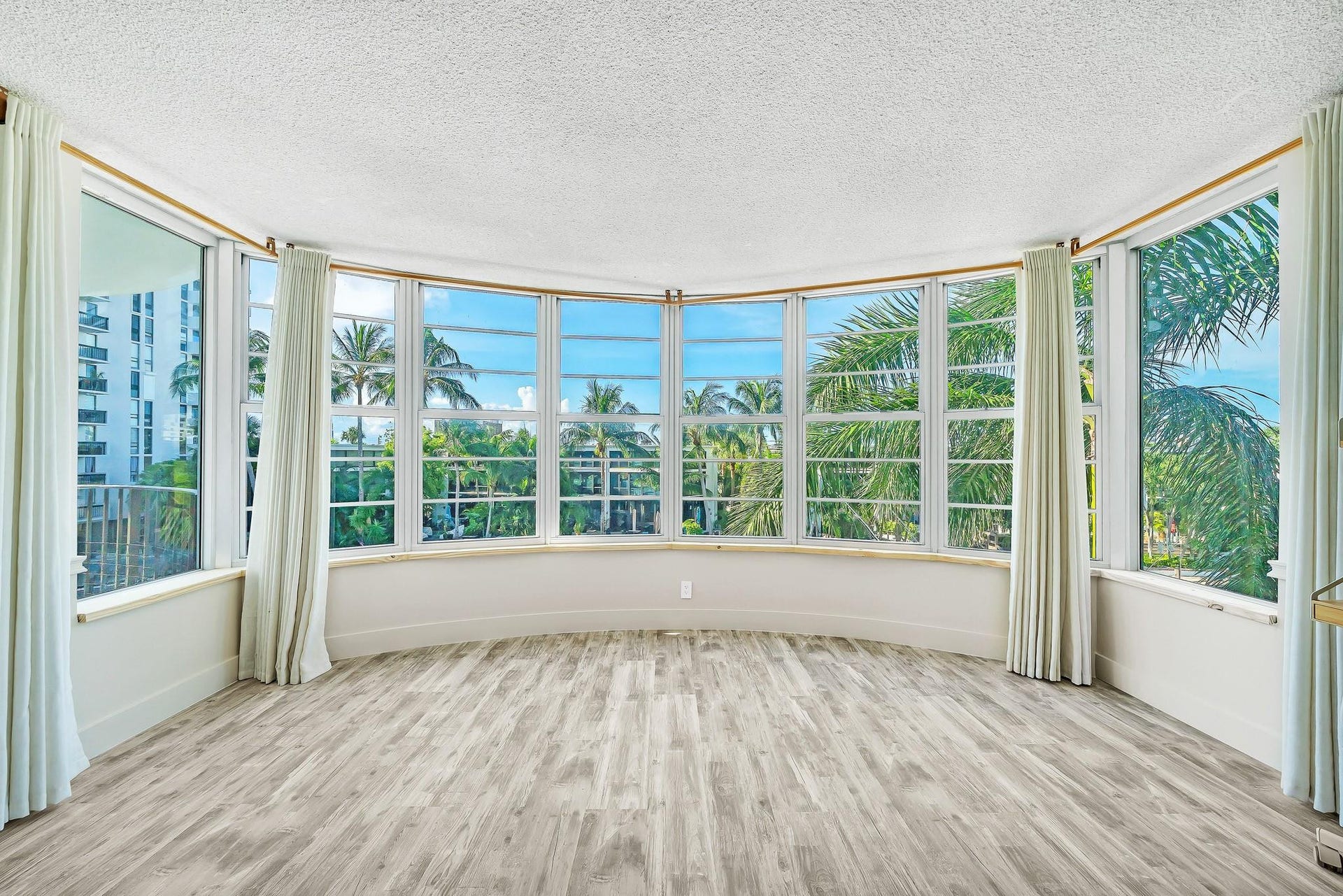 3051 NE 48TH Street, #301, Fort Lauderdale, Fort Lauderdale, FL 33308 Curved wall of windows, light wood-finish flooring, white window frames, tropical scenery, and distant water