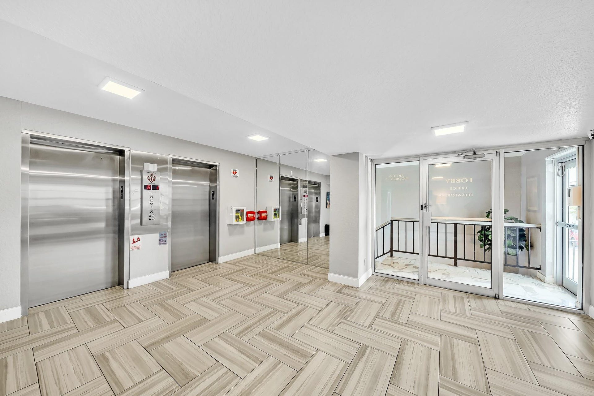 3051 NE 48TH Street, #301, Fort Lauderdale, Fort Lauderdale, FL 33308 Lobby with patterned tile flooring, two stainless steel elevators, mirrored wall accents, and glass-paneled entry doors