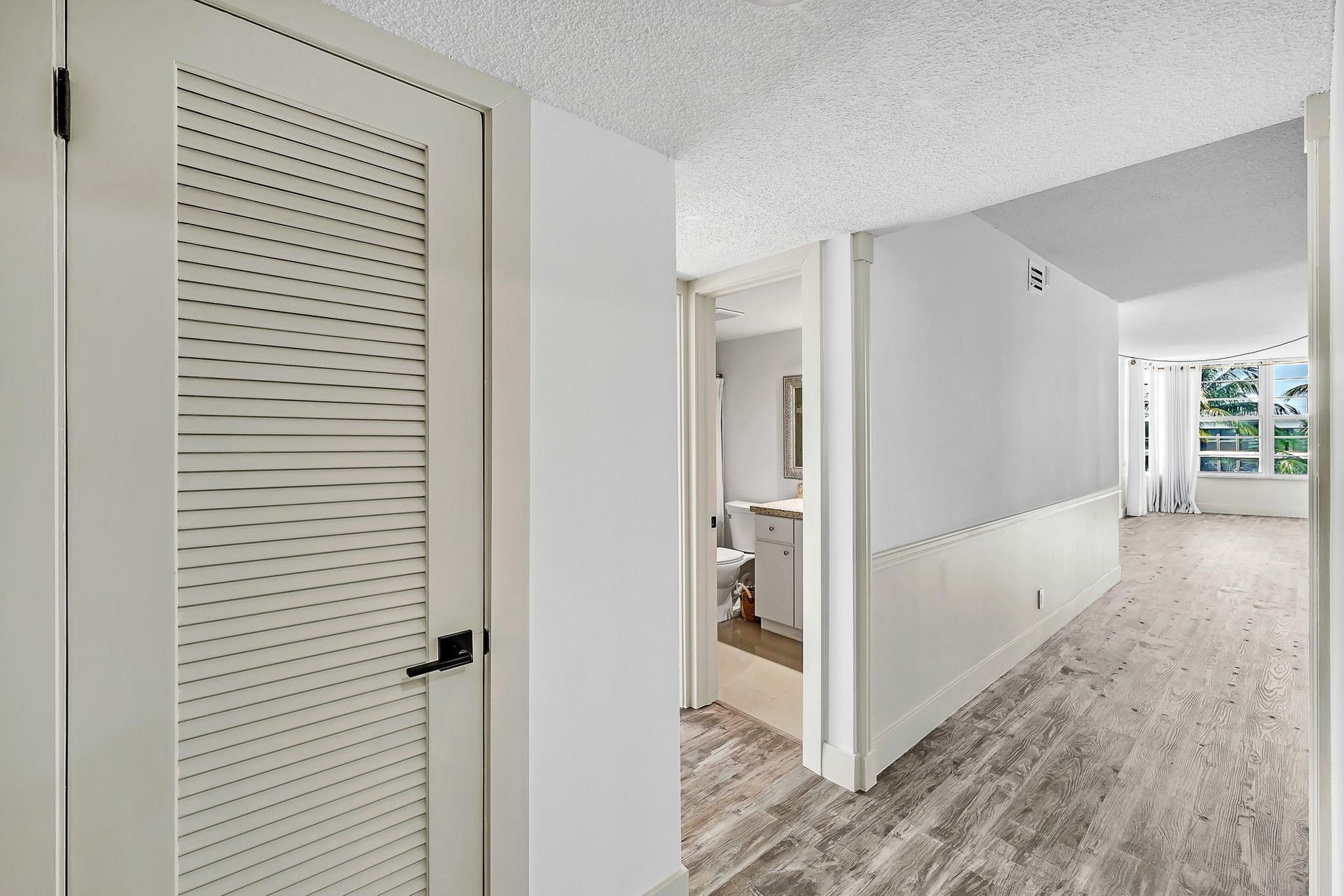 3051 NE 48TH Street, #301, Fort Lauderdale, Fort Lauderdale, FL 33308 Louvered door with black hardware, wood-finish flooring, half wall with paneling, and large windows