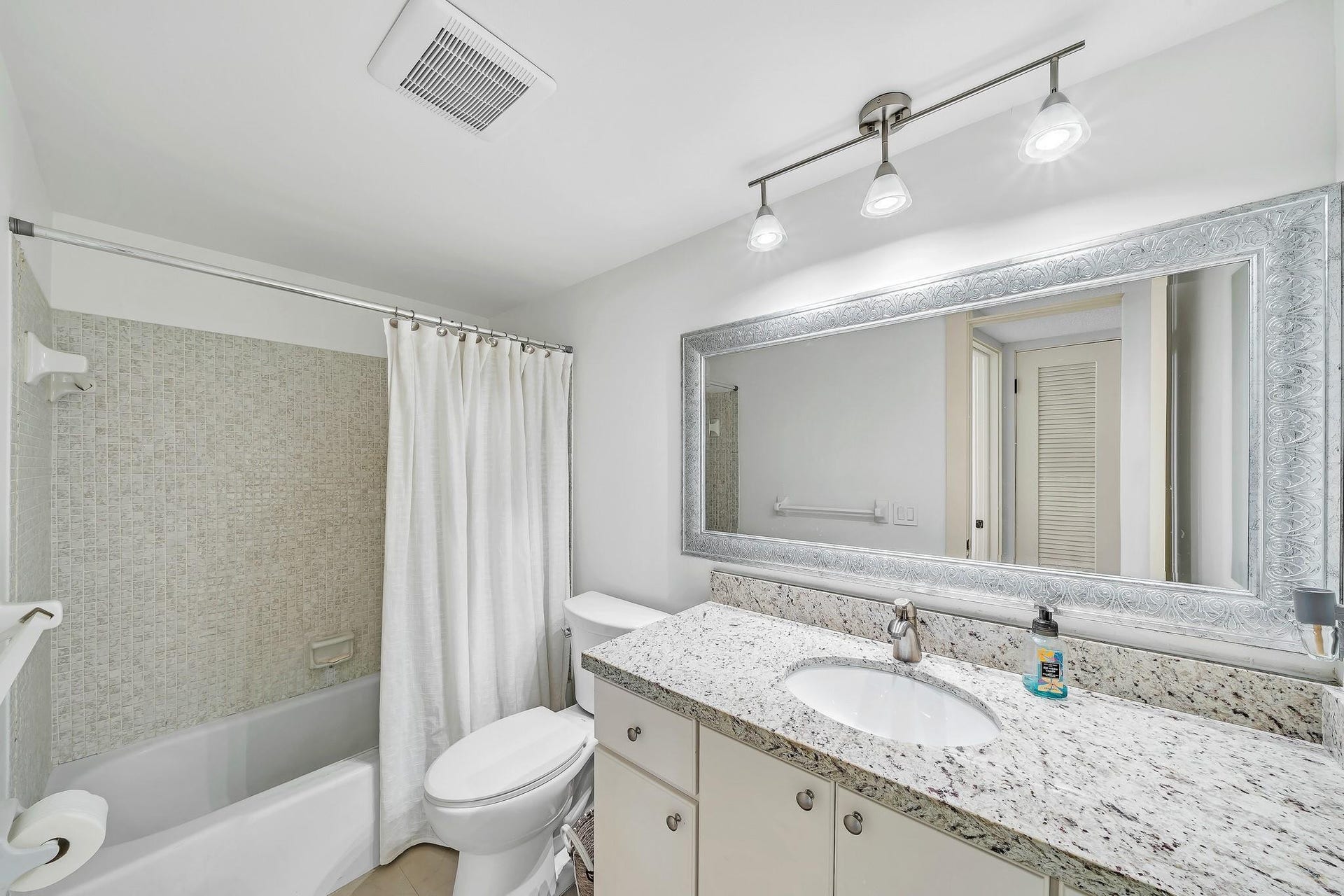 3051 NE 48TH Street, #301, Fort Lauderdale, Fort Lauderdale, FL 33308 Bathroom featuring a vanity with a white-finish cabinet, stone-finish countertop, single basin sink, and framed mirror, along with a tub and shower combination with tile surround