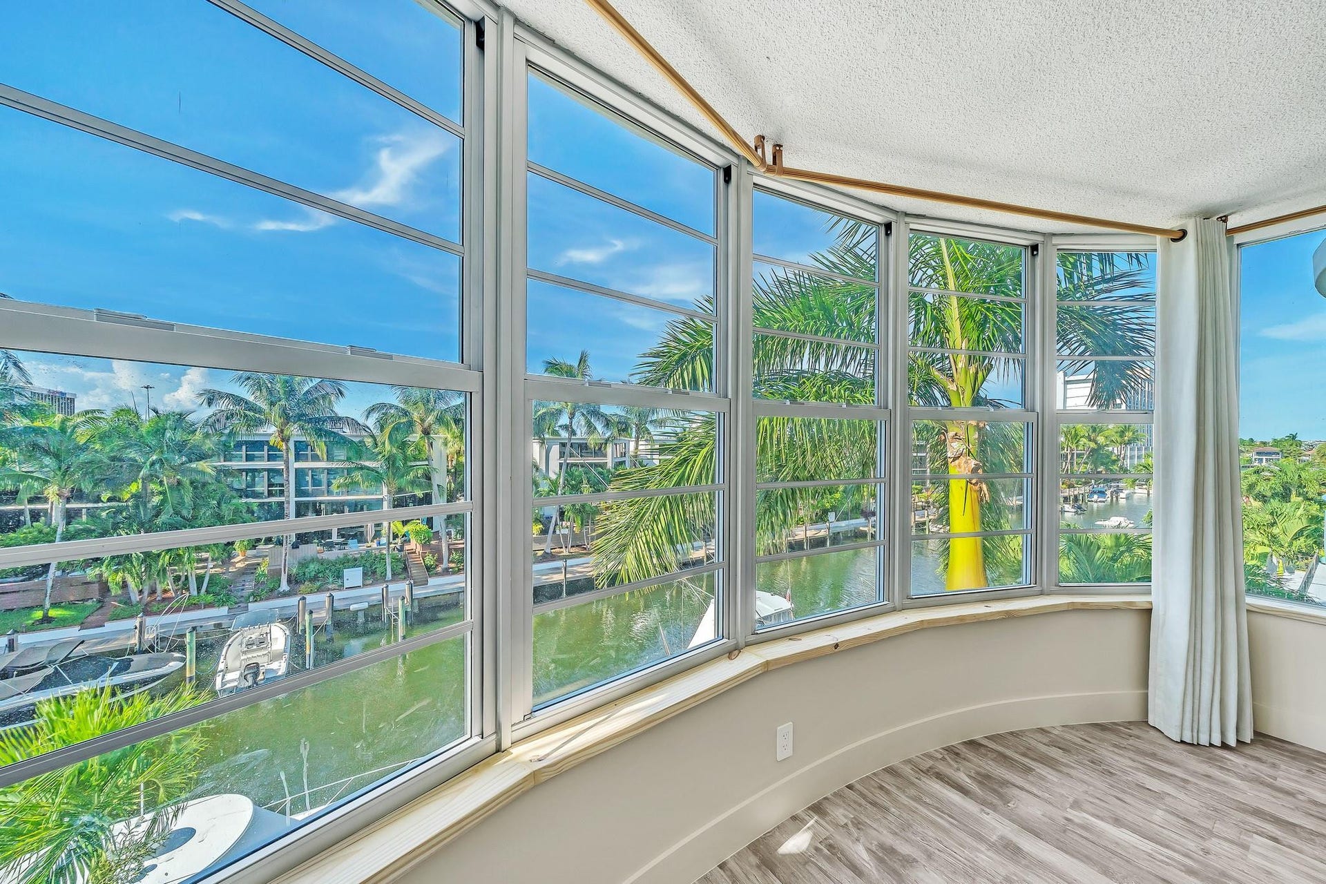 3051 NE 48TH Street, #301, Fort Lauderdale, Fort Lauderdale, FL 33308 Curved window wall with multiple large pane windows, wood-finish flooring, and a waterway background with boats
