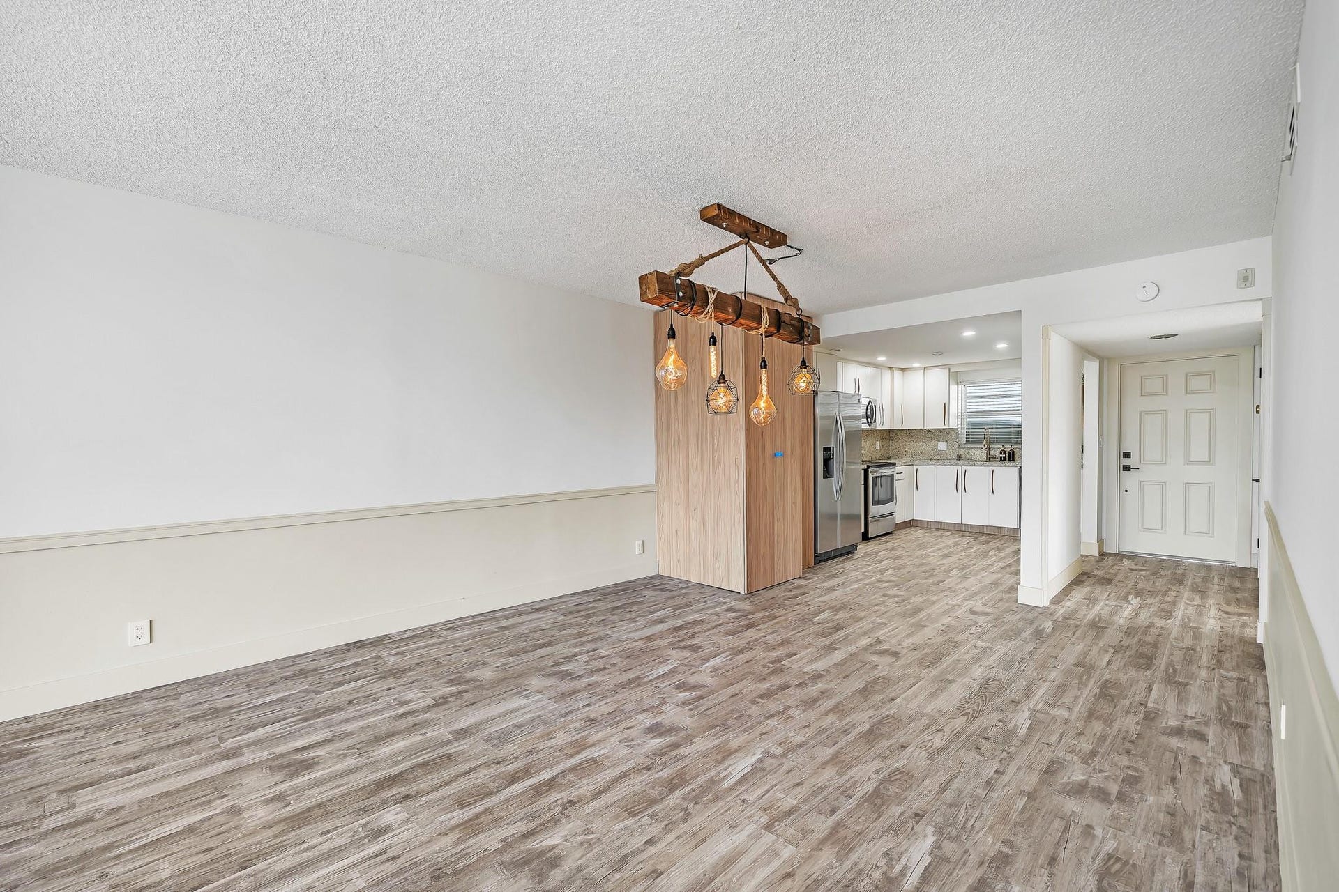 3051 NE 48TH Street, #301, Fort Lauderdale, Fort Lauderdale, FL 33308 Wood-finish flooring throughout, with a recessed kitchen featuring white cabinetry, stainless steel appliances, and a tiled backsplash
