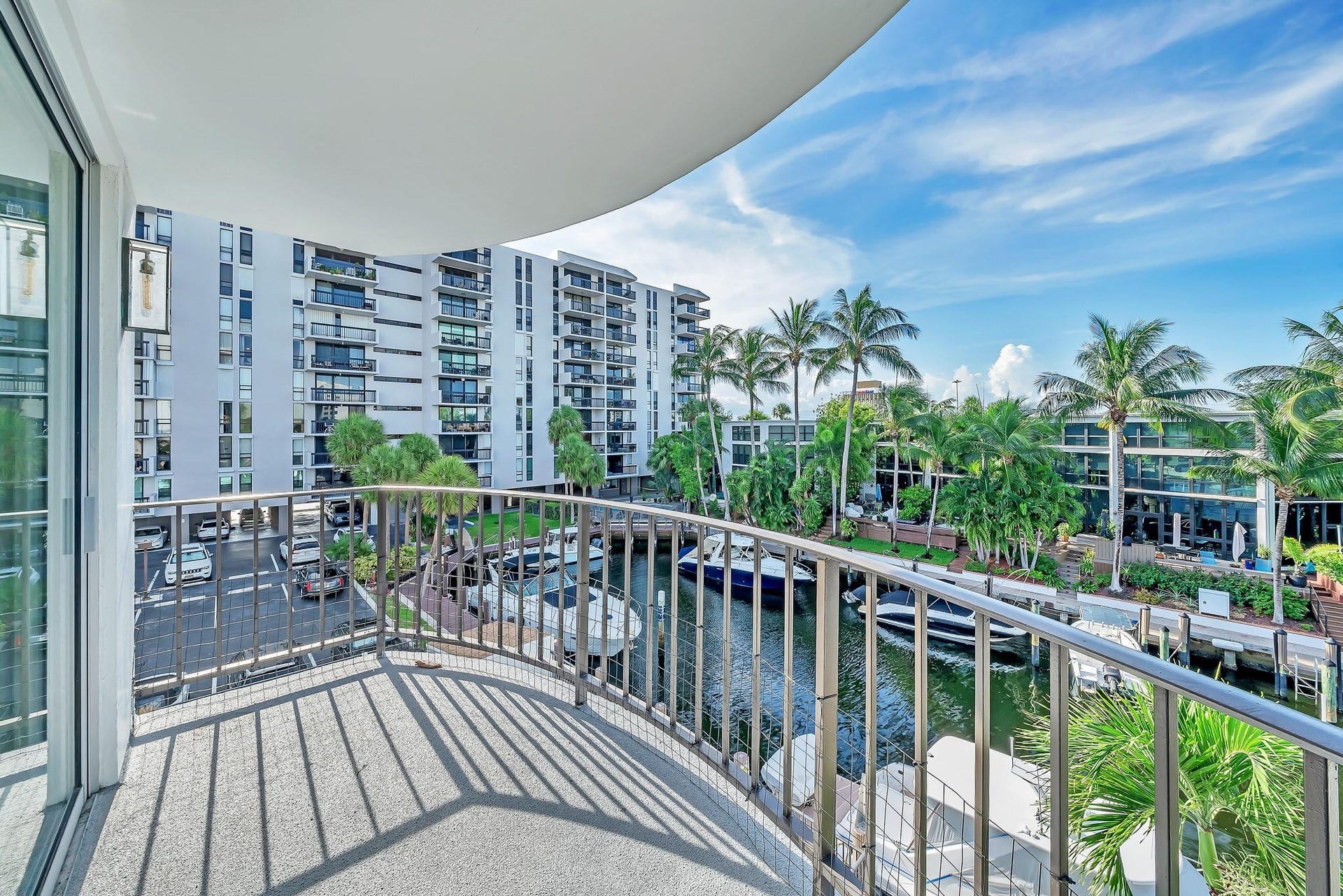 3051 NE 48TH Street, #301, Fort Lauderdale, Fort Lauderdale, FL 33308 Curved balcony with metal railing overlooking a canal with boats, palm trees, and residential buildings