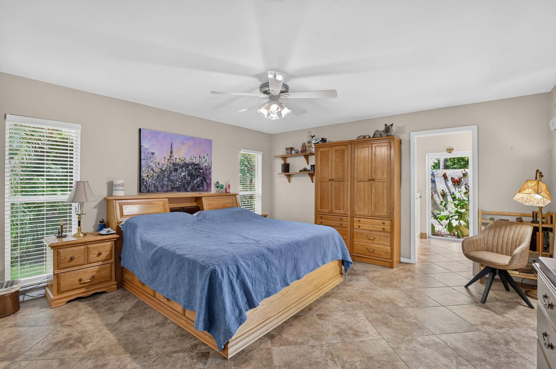Spacious primary bedroom-- neutral wall tones, tile flooring, a ceiling fan with integrated lighting, and multiple windows with blinds