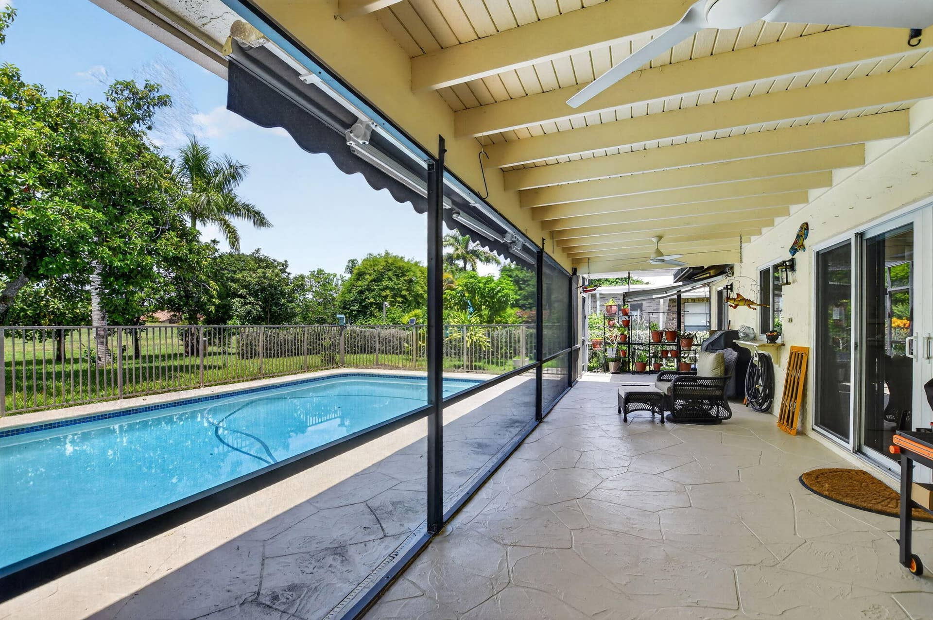 Expansive covered patio with stamped concrete flooring, a built-in swimming pool, a screened enclosure, and multiple ceiling fans