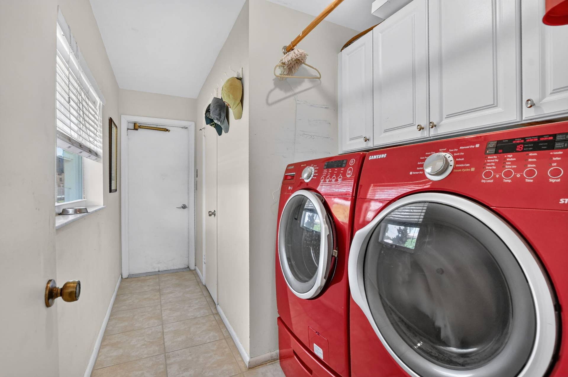 Utility area featuring tile flooring, white upper cabinetry, and a window with blinds
